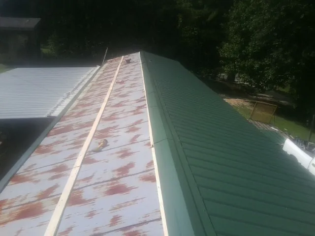 Old rusted panels beside newly installed green metal roofing in Woodbourne
