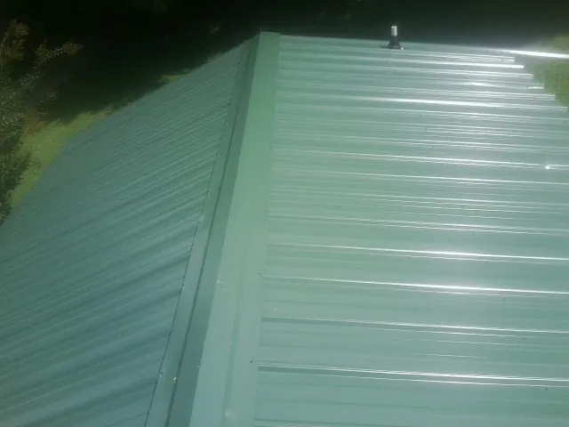 New green metal panels meeting at the ridge of a roof — Flat Roof Repair work by our crew in Woodbourne
