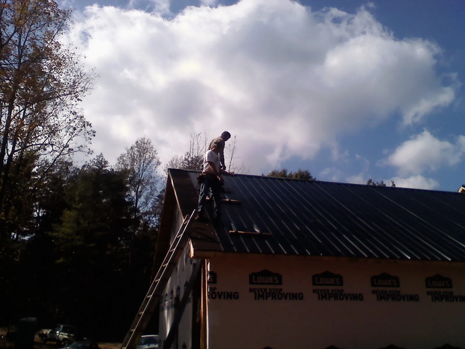 Roofer fastening dark metal panels high against a cloudy sky, from a Roof Inspection job in Woodbourne