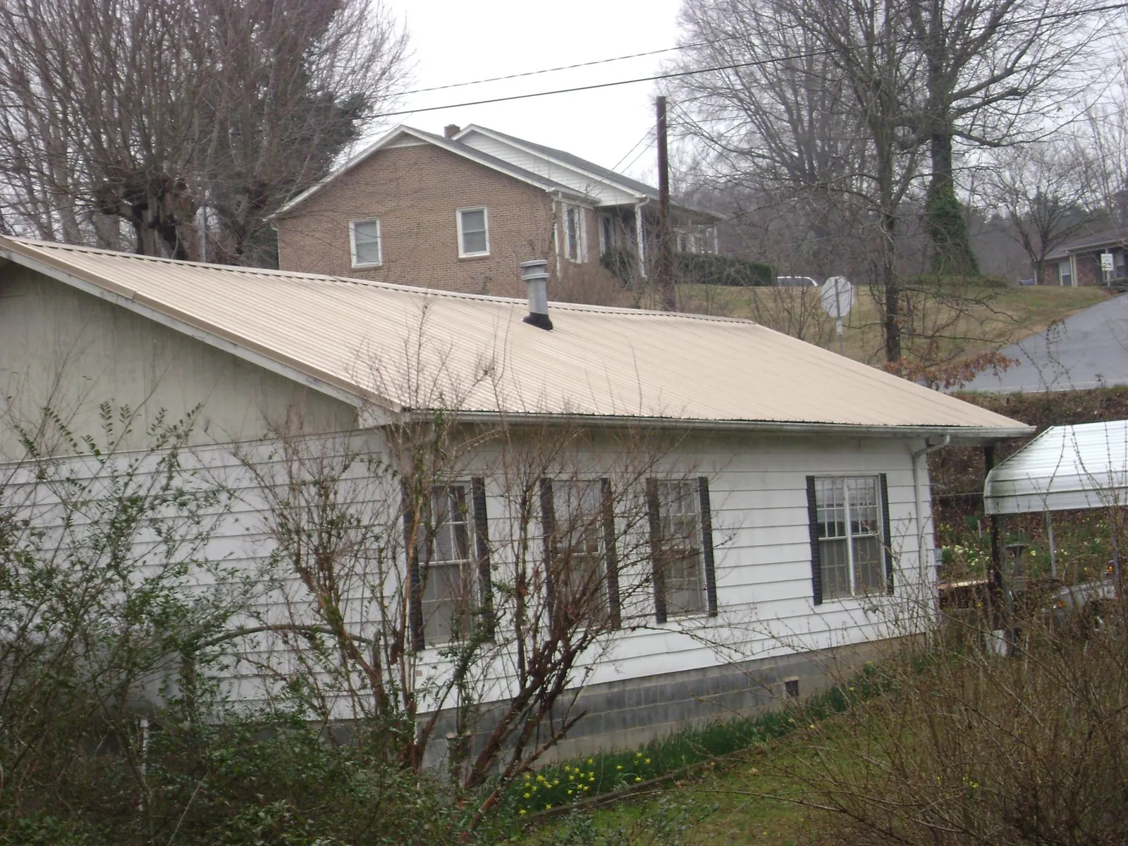 Tan metal roof on a white sided house set into a hillside — Commercial Roofing by Roofing Brothers in Woodbourne