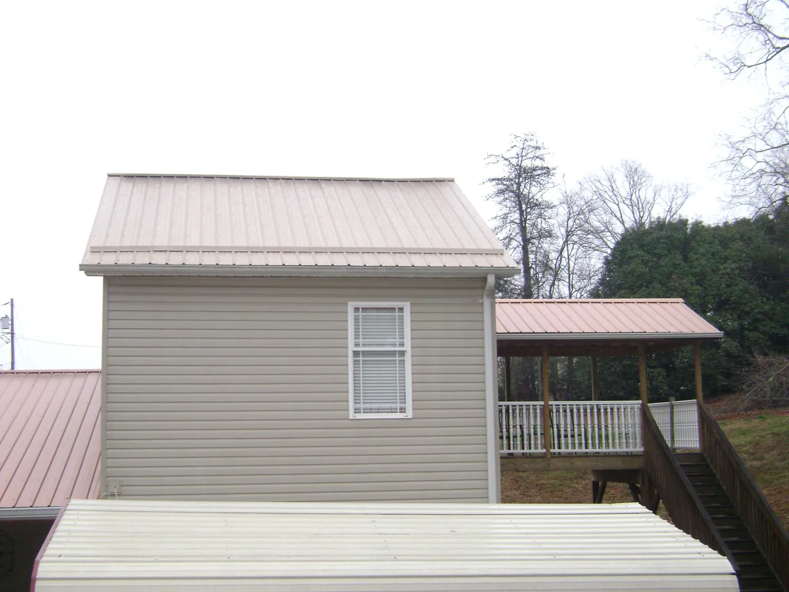 Tan metal roofs on a two story addition and attached porch, from a Roof Replacement job in Woodbourne